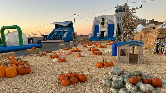 Pumpkins and family attractions spread across the straw at twilight